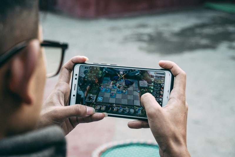 Diverse group of adult gamers in relaxed setting reviewing mobile games on tablets and phones, dark-themed UI visible on screens