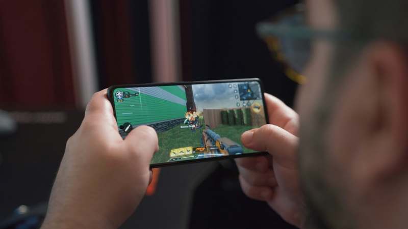 Mobile phone showing a stylized adult-themed mobile game interface with dark theme, neon accents, and controller icon